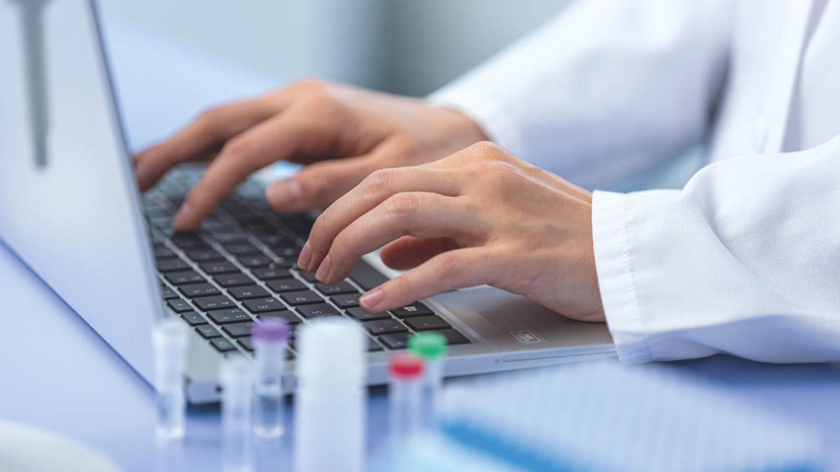 OEM, generic, lab, close up of a selection of vials and someone typing at a laptop in the lab
